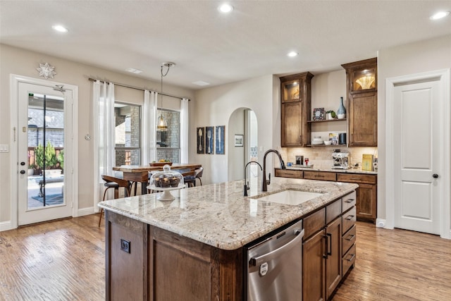 kitchen featuring light wood finished floors, open shelves, arched walkways, a sink, and stainless steel dishwasher