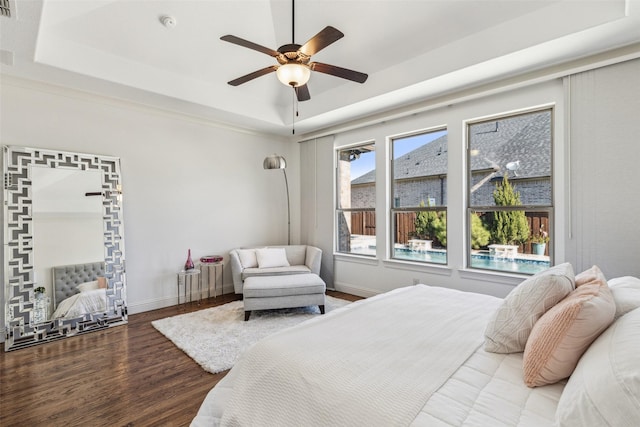 bedroom featuring ceiling fan, a tray ceiling, baseboards, and wood finished floors