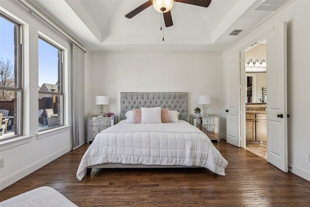 bedroom featuring a tray ceiling, visible vents, baseboards, and wood finished floors