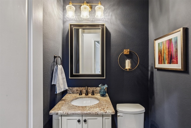 half bathroom with vanity, toilet, and a textured wall