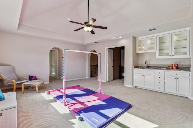 interior space featuring visible vents, arched walkways, a sink, light carpet, and a raised ceiling