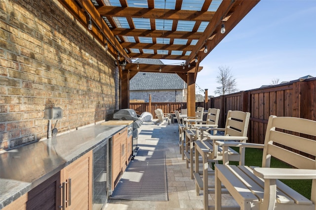 view of patio / terrace featuring a pergola, a fenced backyard, wine cooler, outdoor dining area, and an outdoor kitchen