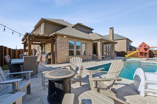 exterior space with a pool with connected hot tub, an outdoor fire pit, a playground, and a fenced backyard