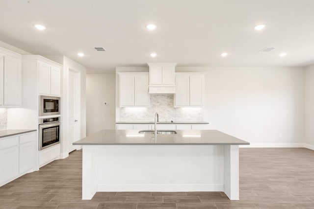329 Sparkling Springs Dr, Waxahachie, TX 75165 - kitchen with a sink, stainless steel oven, light wood-style flooring, an island with sink, and backsplash