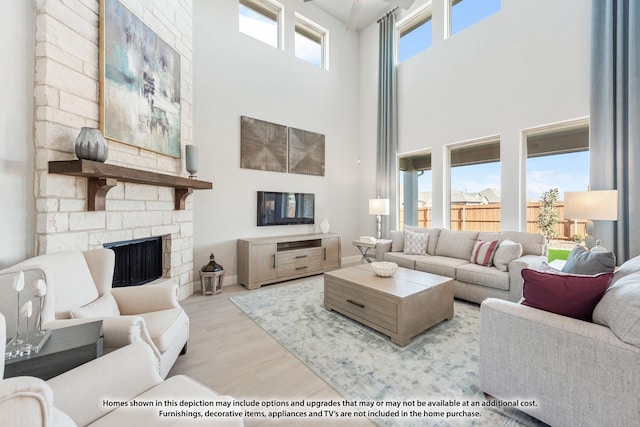 living room with a towering ceiling, light wood-type flooring, and a stone fireplace