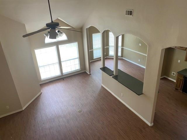 unfurnished living room featuring dark hardwood / wood-style flooring, vaulted ceiling, ceiling fan, and a healthy amount of sunlight