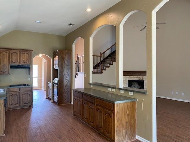 kitchen with ceiling fan, a fireplace, range hood, dark hardwood / wood-style flooring, and gas cooktop