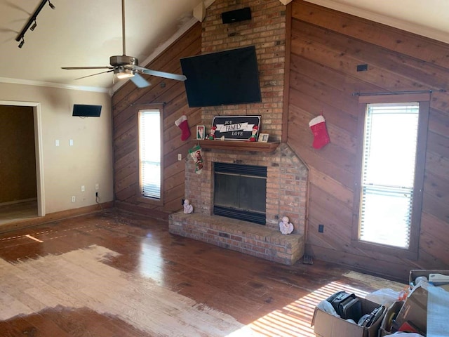 unfurnished living room with a wealth of natural light, wood walls, ceiling fan, and track lighting