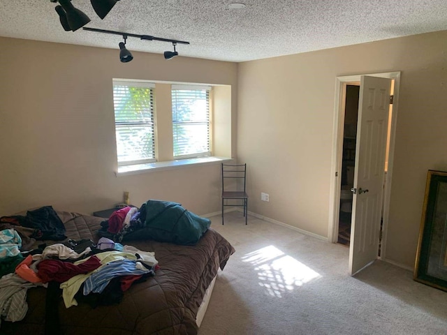 bedroom featuring light colored carpet, a textured ceiling, and track lighting