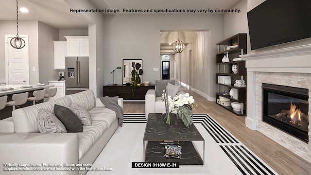 living room featuring a stone fireplace, light hardwood / wood-style flooring, and a chandelier