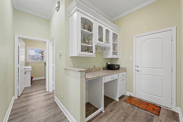 bar with light stone counters, ornamental molding, built in desk, light hardwood / wood-style floors, and white cabinetry