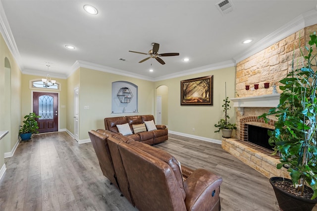 living room with a stone fireplace, hardwood / wood-style floors, ceiling fan with notable chandelier, and ornamental molding