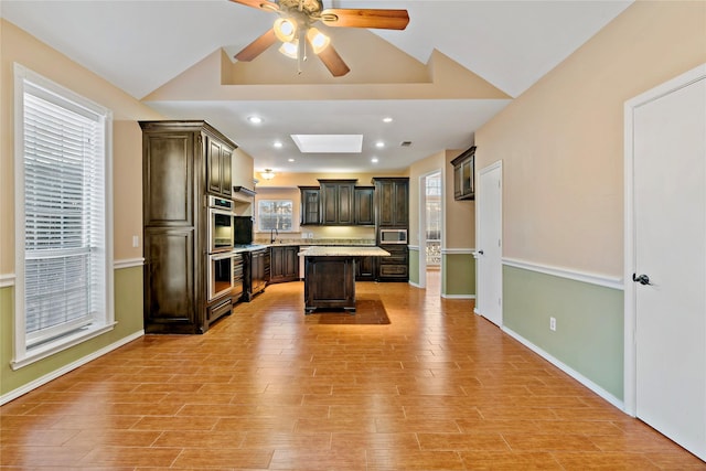 kitchen featuring a center island, appliances with stainless steel finishes, dark brown cabinets, and vaulted ceiling with skylight