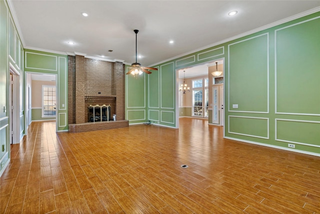 unfurnished living room featuring a fireplace, wood-type flooring, crown molding, and ceiling fan with notable chandelier