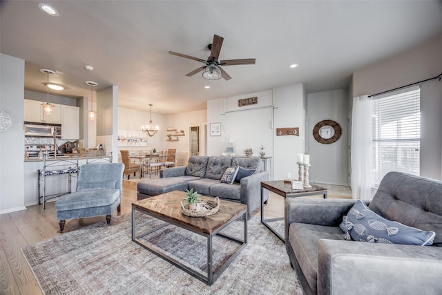 living room featuring ceiling fan with notable chandelier and light wood-type flooring