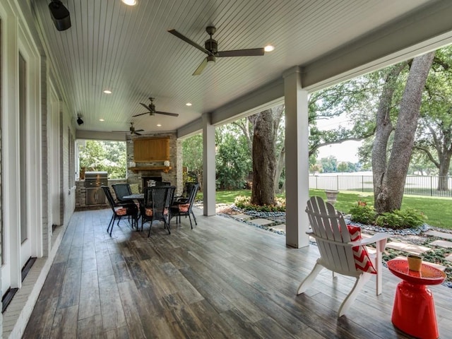 wooden deck featuring an outdoor stone fireplace, an outdoor kitchen, ceiling fan, and a lawn