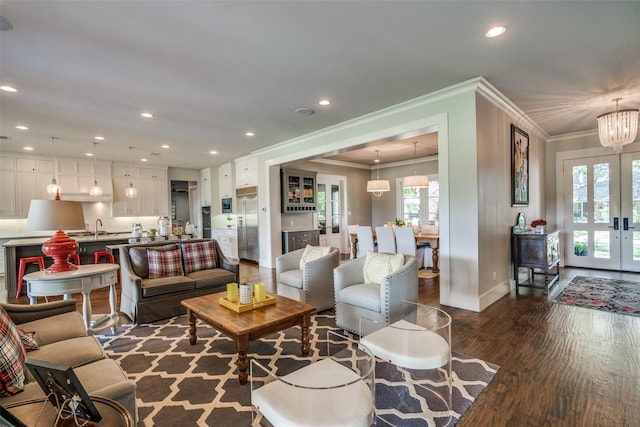 living room featuring dark wood-type flooring, french doors, an inviting chandelier, sink, and ornamental molding