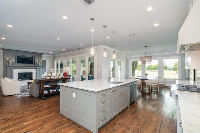 kitchen with custom range hood, light stone counters, pendant lighting, a fireplace, and a center island with sink