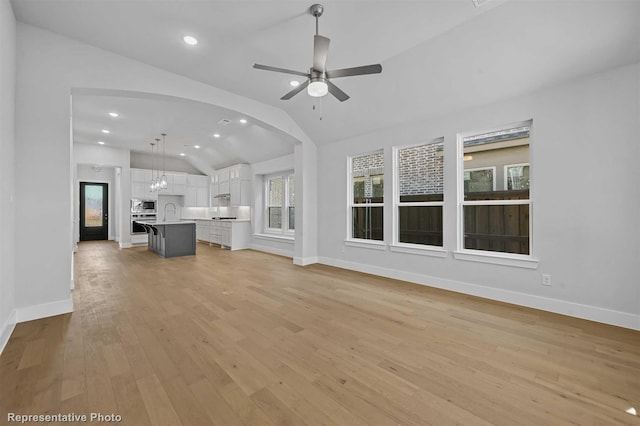 unfurnished living room featuring ceiling fan, vaulted ceiling, sink, and light hardwood / wood-style flooring