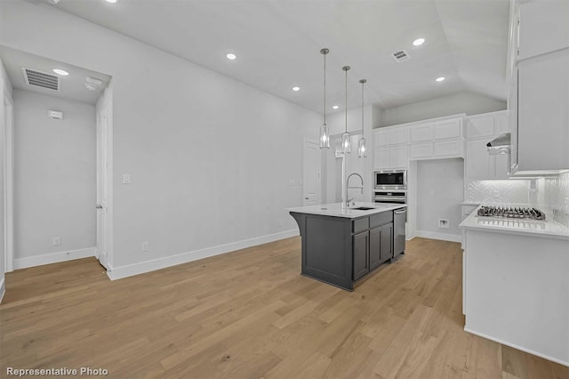 kitchen featuring appliances with stainless steel finishes, white cabinetry, an island with sink, backsplash, and hanging light fixtures