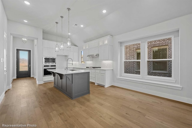 kitchen featuring white cabinetry, a center island with sink, stainless steel appliances, lofted ceiling, and pendant lighting