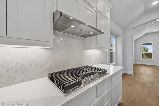 kitchen featuring lofted ceiling, exhaust hood, white cabinetry, tasteful backsplash, and stainless steel gas cooktop