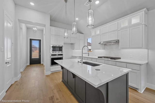 kitchen featuring appliances with stainless steel finishes, a kitchen island with sink, light stone countertops, white cabinets, and sink