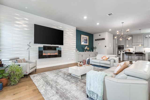 living room with sink, a large fireplace, a chandelier, and light wood-type flooring