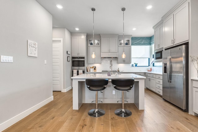 kitchen featuring sink, hanging light fixtures, stainless steel appliances, a center island with sink, and light wood-type flooring