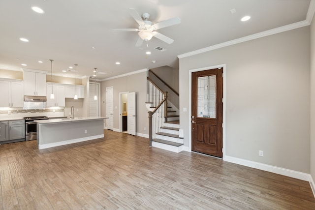 kitchen with stainless steel range oven, sink, pendant lighting, a kitchen island with sink, and white cabinets