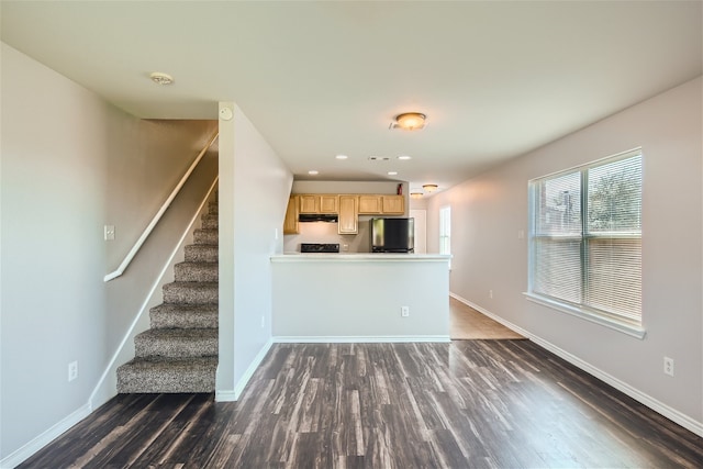 kitchen with light brown cabinetry, dark wood-type flooring, stainless steel fridge, and kitchen peninsula