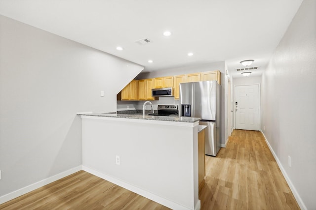 kitchen with appliances with stainless steel finishes, sink, kitchen peninsula, light brown cabinets, and light hardwood / wood-style flooring