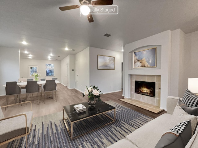 living room featuring a tile fireplace, ceiling fan, and wood-type flooring