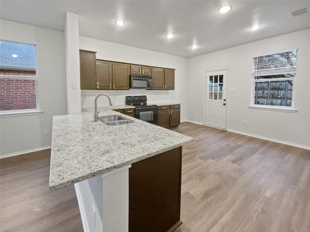 kitchen featuring light stone countertops, dark brown cabinets, sink, black appliances, and hardwood / wood-style flooring