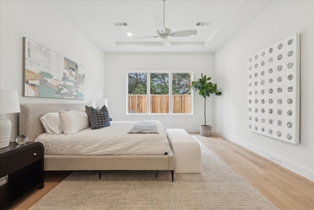 bedroom featuring light wood-type flooring, a tray ceiling, and ceiling fan