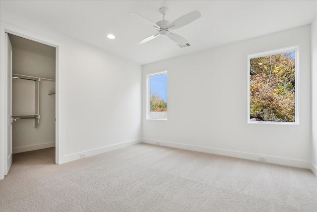 unfurnished bedroom with ceiling fan, a spacious closet, light carpet, and multiple windows