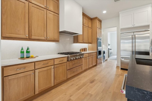 kitchen with dark stone counters, custom range hood, stainless steel appliances, sink, and light hardwood / wood-style flooring