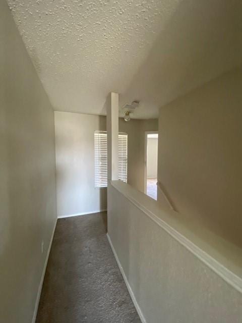 hallway featuring a textured ceiling, baseboards, and carpet floors
