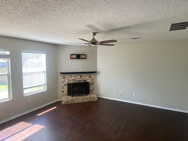 unfurnished living room with a textured ceiling, ceiling fan, visible vents, wood finished floors, and a fireplace