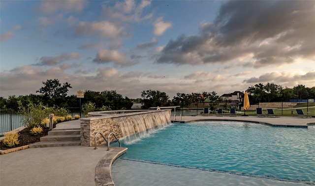 pool at dusk featuring pool water feature and a patio area