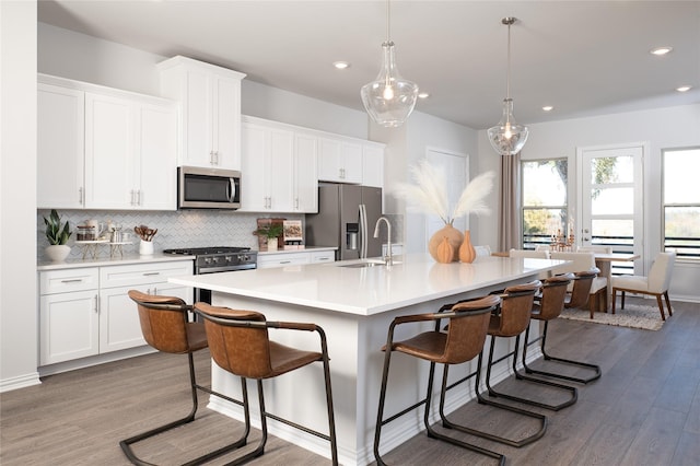 kitchen with a kitchen bar, an island with sink, white cabinets, and stainless steel appliances