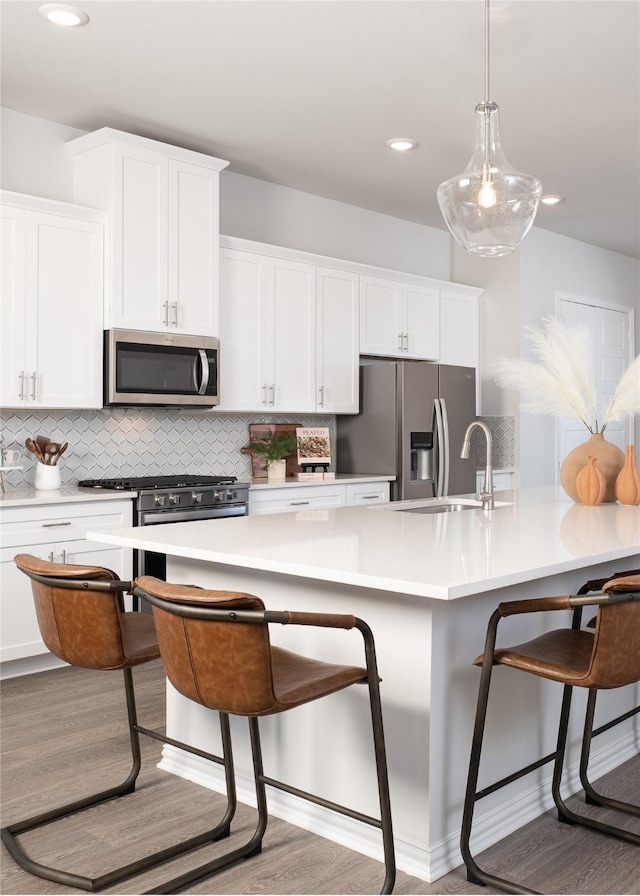 kitchen with a kitchen bar, white cabinetry, stainless steel appliances, and light hardwood / wood-style flooring