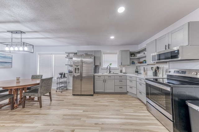 kitchen with pendant lighting, a textured ceiling, gray cabinets, appliances with stainless steel finishes, and light wood-type flooring