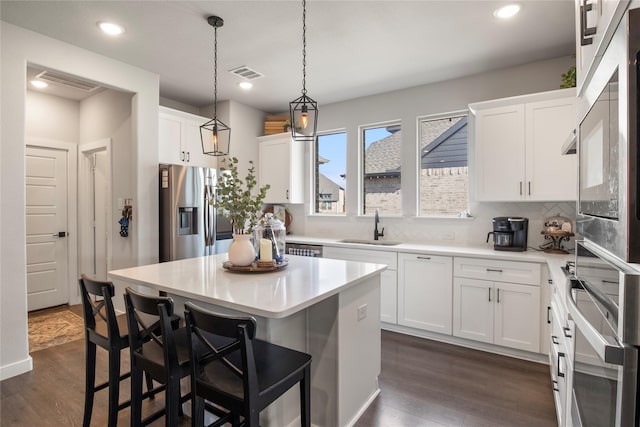 kitchen with dark wood-type flooring, stainless steel appliances, white cabinetry, and a center island