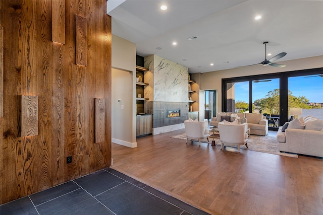 unfurnished living room featuring a tile fireplace, built in shelves, ceiling fan, and dark wood-type flooring