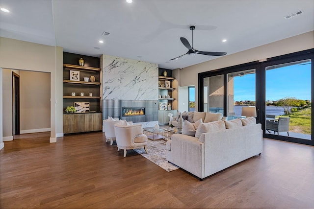 living room with built in shelves, ceiling fan, hardwood / wood-style floors, and a fireplace