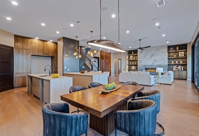 dining room with light wood-type flooring, built in shelves, ceiling fan, sink, and a premium fireplace