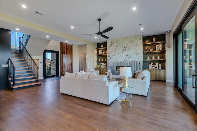 living room with wood-type flooring, built in features, ceiling fan, and a premium fireplace