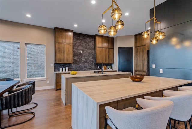 kitchen featuring hanging light fixtures, tasteful backsplash, a kitchen bar, a kitchen island with sink, and light wood-type flooring