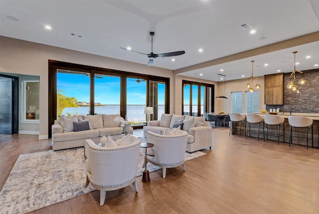 living room with a water view, light hardwood / wood-style floors, and ceiling fan with notable chandelier